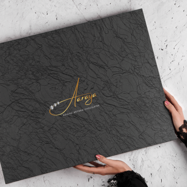 Indulge in Aaraya Chocolates' Luxury Noir Box – a curated selection of signature chocolates, cocoa bars, truffles, scented candles, and non-alcoholic champagne. Immerse yourself in the opulence of fine chocolate craftsmanship, with rich flavors and exquisite aromas.