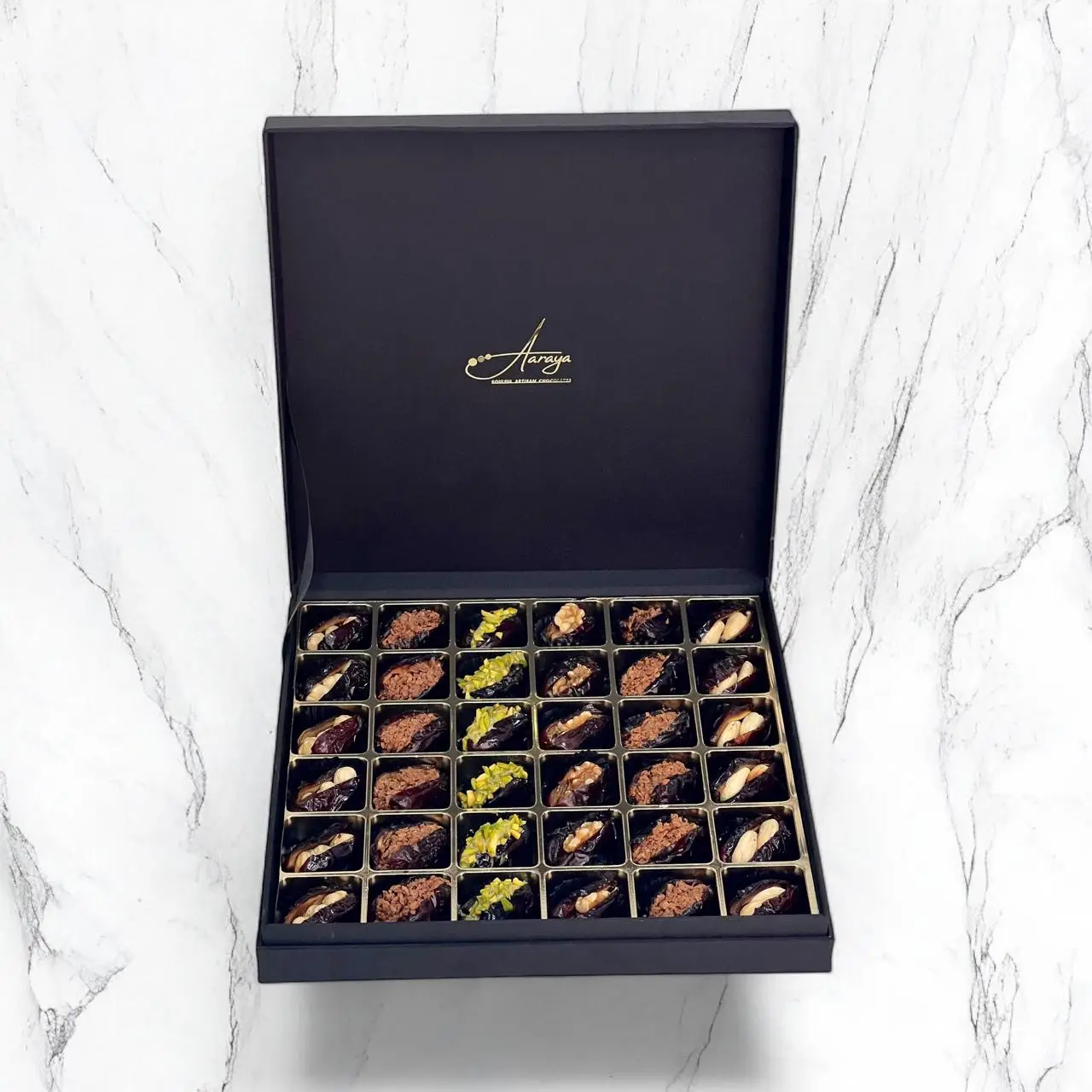 An exquisite assortment of Assorted Luxury Dates by Aaraya Chocolates, showcasing a symphony of premium flavors including Lemon Peel, Pistachio, Orange Peel, Cashew Nut, Salted Hazelnut, Feuilletine Crunch, Walnut, Almond Blanched, and Pistachio Ganache. Each date is a masterpiece of indulgence, promising a sensory journey through the finest gourmet fillings.