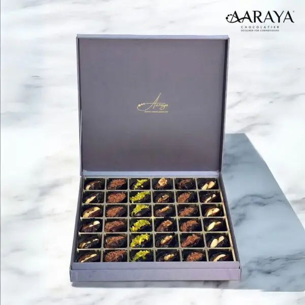 An exquisite assortment of Assorted Luxury Dates by Aaraya Chocolates, showcasing a symphony of premium flavors including Lemon Peel, Pistachio, Orange Peel, Cashew Nut, Salted Hazelnut, Feuilletine Crunch, Walnut, Almond Blanched, and Pistachio Ganache. Each date is a masterpiece of indulgence, promising a sensory journey through the finest gourmet fillings.