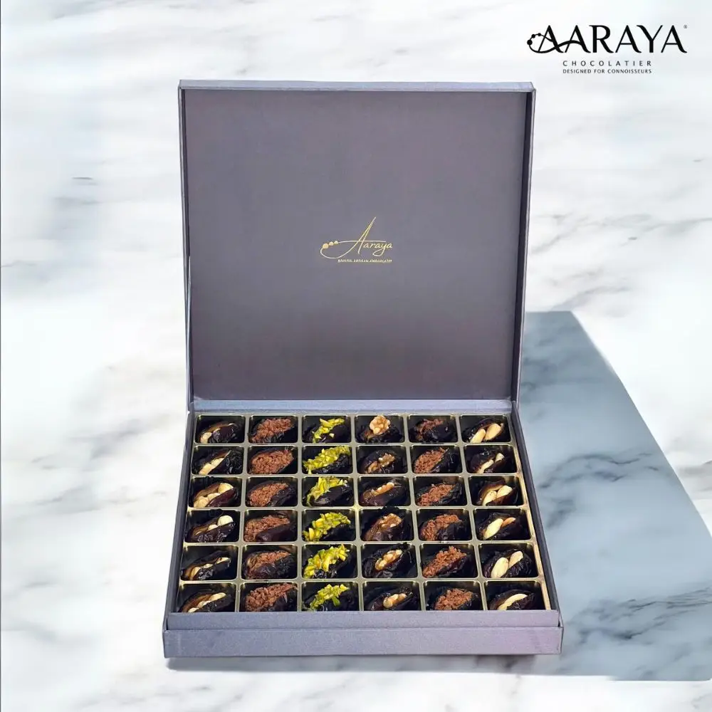 An exquisite assortment of Assorted Luxury Dates by Aaraya Chocolates, showcasing a symphony of premium flavors including Lemon Peel, Pistachio, Orange Peel, Cashew Nut, Salted Hazelnut, Feuilletine Crunch, Walnut, Almond Blanched, and Pistachio Ganache. Each date is a masterpiece of indulgence, promising a sensory journey through the finest gourmet fillings.