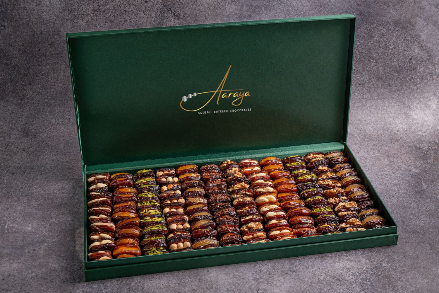 An exquisite assortment of Assorted Luxury Dates by Aaraya Chocolates, showcasing a symphony of premium flavors including Lemon Peel, Pistachio, Orange Peel, Cashew Nut, Salted Hazelnut, Feuilletine Crunch, Walnut, Almond Blanched, and Pistachio Ganache. Each date is a masterpiece of indulgence, promising a sensory journey through the finest gourmet fillings.