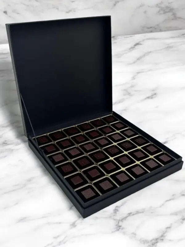 Elegant Noir Indulgence - 70% Dark Chocolate Box displayed on a luxurious white marble table, featuring rich, velvety dark chocolates in sleek black packaging.