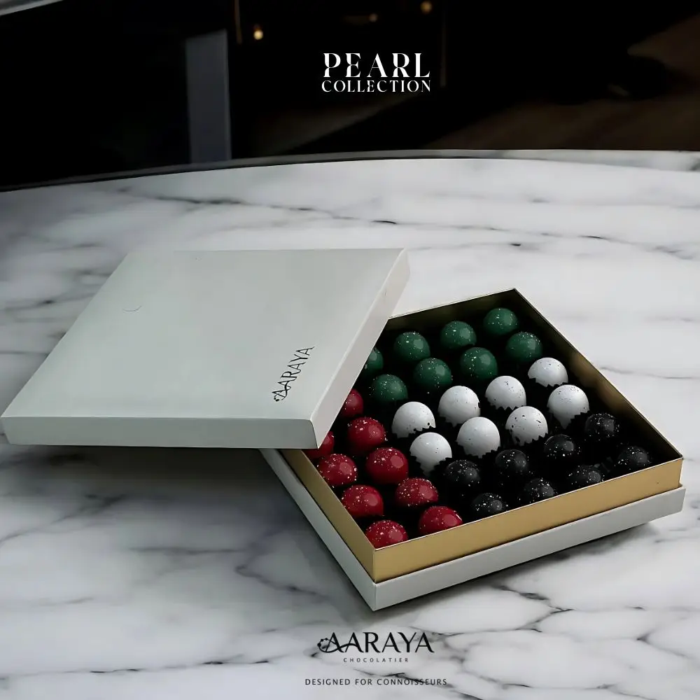 Elegant Pearl Collection by AARAYA® Chocolatier for UAE National Day, inspired by the UAE's rich pearl diving heritage. The 20 cm x 20 cm box contains 36 handcrafted premium chocolates, weighing a total of 700 grams, including 500 grams of artisanal chocolates. Celebrating tradition, unity, and luxury. Available for AED 399